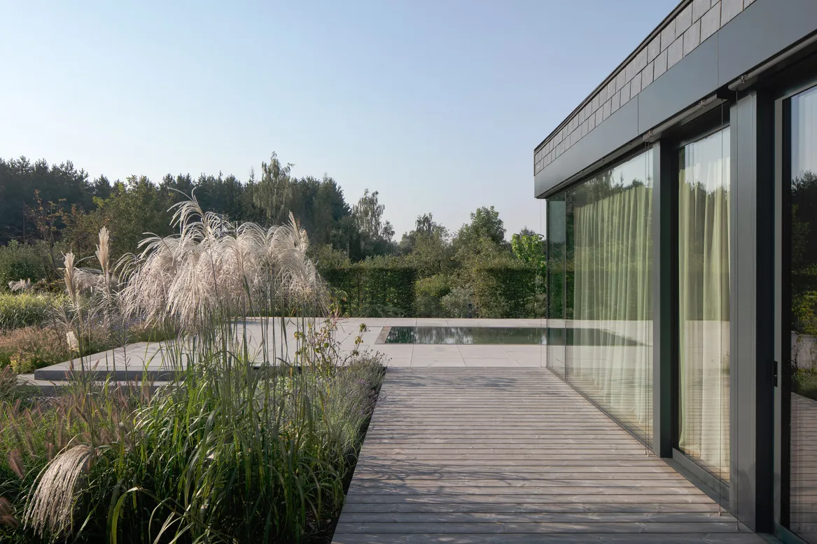 Taras z thermodrewna i basen. Po lewej stronie miskant chiński, w tle żywopłot z graba. Rabaty trawiasto-bylinowe. fot. Piotr Krajewski