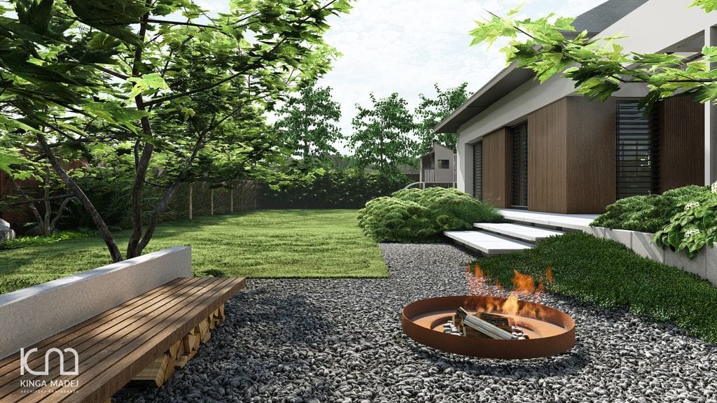 Strefa ogniska z drewnianą ławą. Ciemny żwir. W tyle wielofunkcyjny domek dziecięcy.