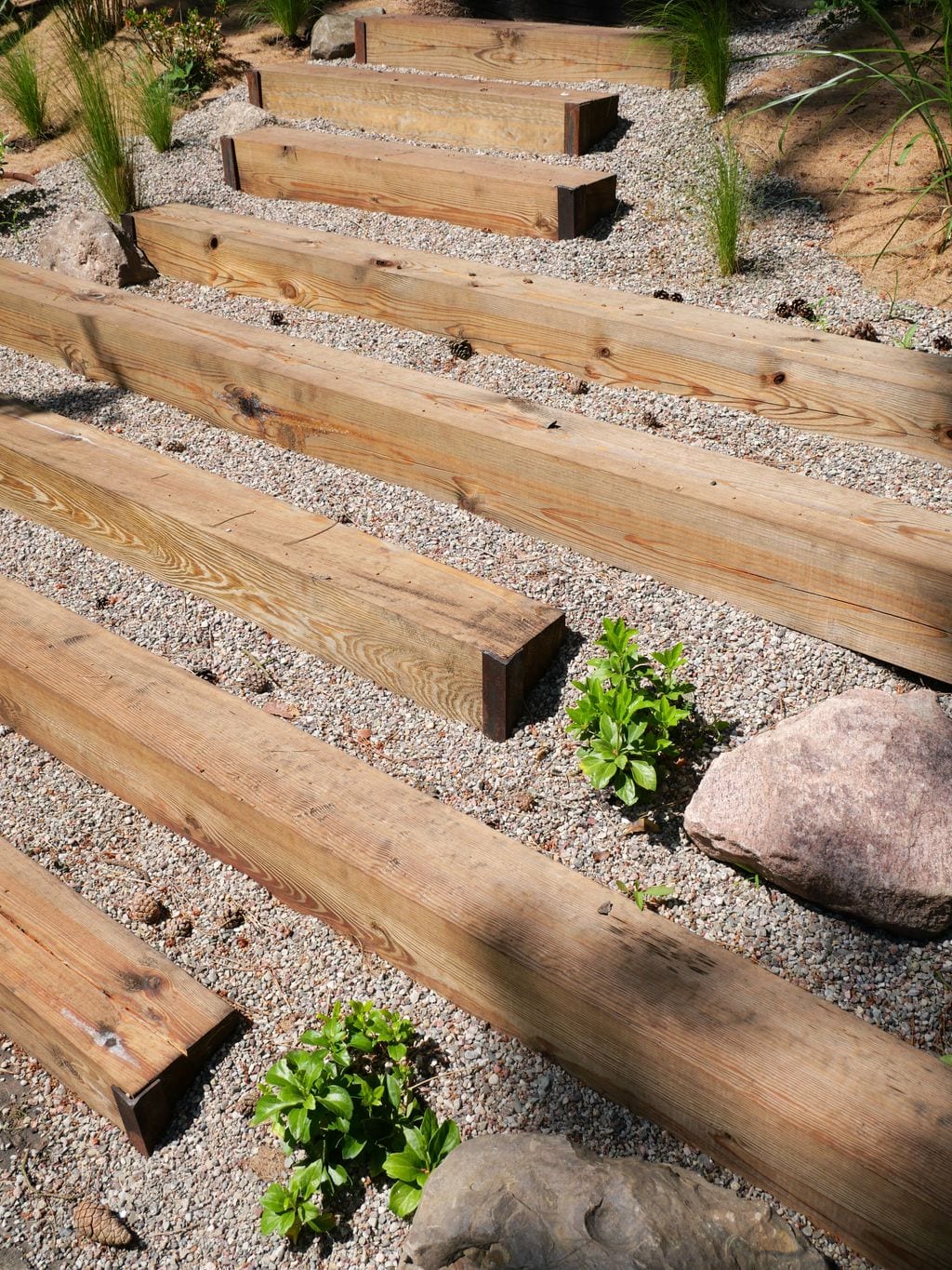 Stopnie z podkładów kolejowych na skarpie prowadzące do tylnego wyjścia. Żwir, głazy, runianka, stipy, mata kokosowa.